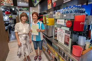 PASTIKAN SINGAPURA BERSIH BERSAMA: Penyelia kedai kopi Clementi 881, Cik Heng Siew Hieok (kanan), menerima tanda pelekat 'SG Clean' daripada Dr Amy Khor. - Foto NEA