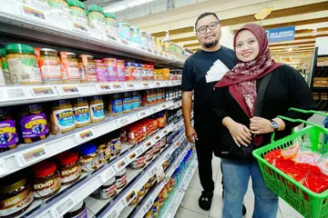 Encik Muhammad Nurherrizzwan Shah Kamin, 44 tahun (kiri),  dan isteri, Cik Nooraihana Abdul Rahman, 38 tahun (kanan) di cawangan NTUC FairPrice Our Tampines Hub (OTH) semasa Sabtu semasa berbelanja bagi memenuhi keperluan lima anak mereka.