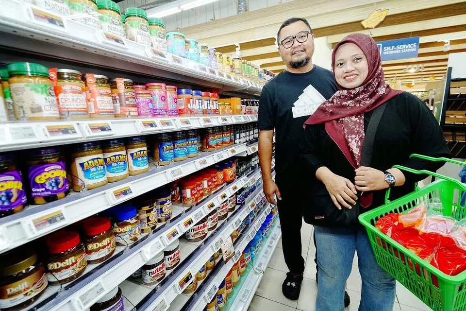 Encik Muhammad Nurherrizzwan Shah Kamin, 44 tahun (kiri),  dan isteri, Cik Nooraihana Abdul Rahman, 38 tahun (kanan) di cawangan NTUC FairPrice Our Tampines Hub (OTH) semasa Sabtu semasa berbelanja bagi memenuhi keperluan lima anak mereka.