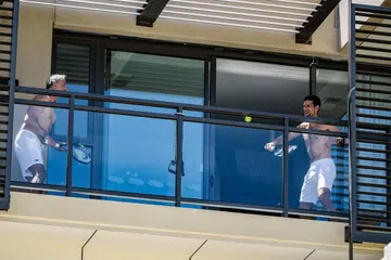 KENA KUARANTIN, BERLATIH DI BALKONI: Pemain tenis nombor satu dunia Novak Djokovic (kanan) berlatih di balkoni bilik hotel dengan seorang kakitangannya di Hotel M Suites di North Adelaide, Adelaide, Australia Selatan. - Foto AFP 