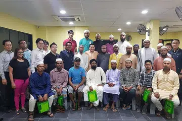 USAHA BERTERUSAN: Ustaz Leyaket Ali Mohamed Omar, anggota RRG (barisan kedua, dengan kain sandang), bergambar dengan pekerja asing dan pegawai kanan dari Kementerian Ehwal Dalam Negeri, termasuk Setiausaha Parlimen Kanan Encik Amrin Amin (barisan kedua, tengah) di satu perjumpaan. - Foto RRG