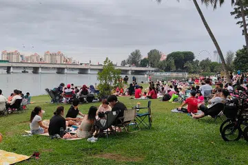 Keluarga berkelah di Kallang Riverside Park sementara menunggu langit menjadi gelap dan pertunjukan bunga api bermula.