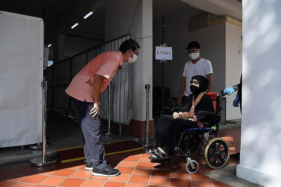 JALANI UJIAN SWAB: Anggota Parlimen GRC Nee Soon, Profesor Madya Dr Muhammad Faishal Ibrahim (kiri), berinteraksi dengan Cik Sokdah Sidang (berkerusi roda) yang turut menjalani ujian swab wajib bersama semua penduduk di Blok 745, Yishun Street 72 semalam bagi membendung penularan Covid-19. Cik Sokdah ditemani anaknya, Encik Zaki Isaac Ahmad (baju-T putih). - Foto BH oleh DESMOND FOO