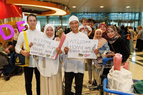 Encik Azman Sahari (tiga dari kiri) dan isterinya, Cik Ame Rohani Sitepu (dua dari kiri), bergambar bersama ahli keluarga mereka di balai ketibaan Terminal 3 Lapangan Terbang Changi pada 1 Jun, sambil memegang poster yang disediakan oleh keluarga sebagai tanda sambutan kepulangan selepas menunaikan ibadah haji.