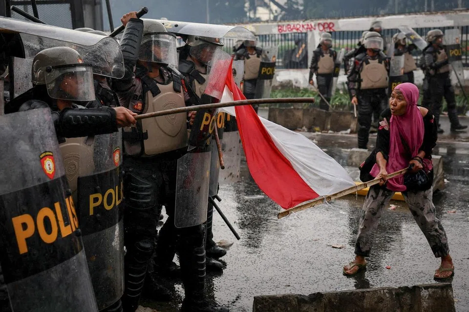 Seorang wanita mengibarkan bendera Indonesia ke arah anggota polis rusuhan semasa pertempuran kecil tercetus dalam satu protes menentang apa yang disifatkan penunjuk perasaan sebagai elaun ahli Parlimen Indonesia yang terlalu tinggi, di luar bangunan Parlimen Indonesia di Jakarta pada 28 Ogos.
