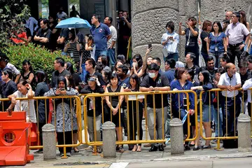 TANDA HORMAT: Berbekal payung dan pelitup, orang ramai yang berhimpun di sepanjang Collyer Quay, berdekatan dengan bangunan Pusat NTUC, menanti dengan sabar di bawah terik suria dan kabut jerebu demi menyambut Perarakan Pengebumian Negara. - Foto TUKIMAN WARJI