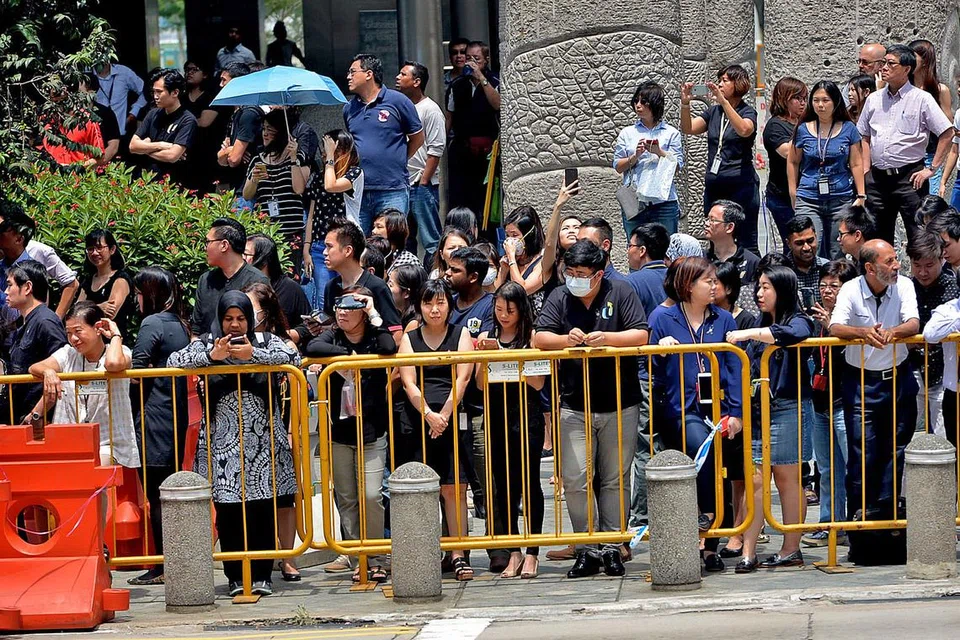 TANDA HORMAT: Berbekal payung dan pelitup, orang ramai yang berhimpun di sepanjang Collyer Quay, berdekatan dengan bangunan Pusat NTUC, menanti dengan sabar di bawah terik suria dan kabut jerebu demi menyambut Perarakan Pengebumian Negara. - Foto TUKIMAN WARJI
