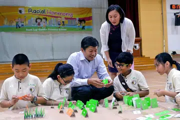 PUPUK DAYA TAHAN PELAJAR: Encik Ng, dengan diperhatikan pengetua Sekolah Rendah Boon Lay Gardens, Cik Ong Loh Jia Miin, berbincang dengan murid-murid mengenai konsep membina 'rumah' menggunakan kad, yang bertujuan melihat semangat daya tahan pelajar melindungi 'rumah' mereka daripada dipukul badai atau gempa bumi. - Foto KHALID BABA