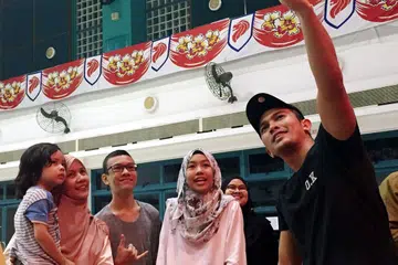 SAMBIL MENYELAM MINUM AIR: Beberapa peminat pelakon popular Malaysia, Saharul Ridzwan (kanan), bergambar bersama bintang pujaan itu selepas membeli kuih Raya di Kelab Masyarakat Toa Payoh West. - Foto SR TIGERS
