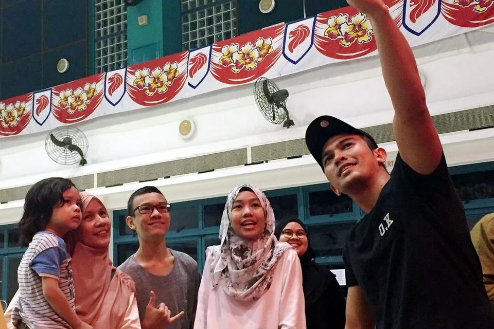 SAMBIL MENYELAM MINUM AIR: Beberapa peminat pelakon popular Malaysia, Saharul Ridzwan (kanan), bergambar bersama bintang pujaan itu selepas membeli kuih Raya di Kelab Masyarakat Toa Payoh West. - Foto SR TIGERS