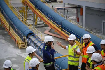 Menteri Pembangunan Negara, Encik Desmond Lee (empat dari kanan), melihat laluan penghantar Pelabuhan Jurong semasa meninjau ekosistem baru konkrit siap dicampur.