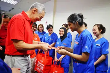 Perdana Menteri, Encik Lee Hsien Loong (kiri), memberi beg sagu hati mengandungi buah oren, keropok, ‘hongbao’ daripada NTUC dan set cawan teh kepada jururawat, karyawan kesihatan bersekutu, doktor serta kakitangan lain Hospital Besar Ng Teng Fong (NTFGH) dan Hospital Masyarakat Jurong (JCH) pada 9 Februari.