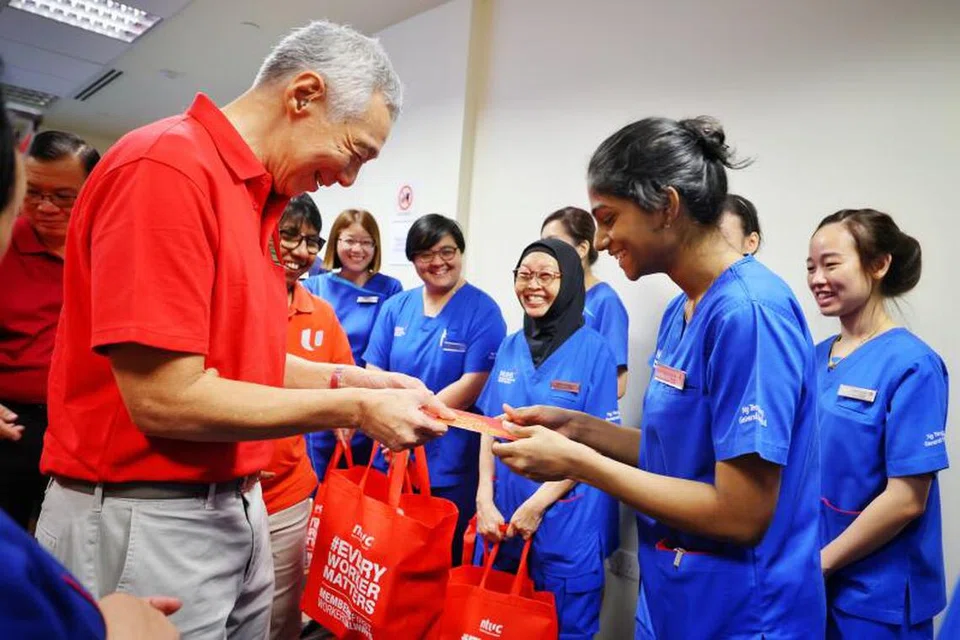 Perdana Menteri, Encik Lee Hsien Loong (kiri), memberi beg sagu hati mengandungi buah oren, keropok, ‘hongbao’ daripada NTUC dan set cawan teh kepada jururawat, karyawan kesihatan bersekutu, doktor serta kakitangan lain Hospital Besar Ng Teng Fong (NTFGH) dan Hospital Masyarakat Jurong (JCH) pada 9 Februari.