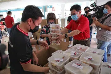 BUNGKUS MAKANAN GERAI PENJAJA: DPM Heng (tiga dari kanan) dan Cik Amy Khor membungkus beberapa bungkusan makanan untuk diedarkan kepada pekerja barisan depan di Hospital Besar Changi. - Foto BH oleh KEVIN LIM