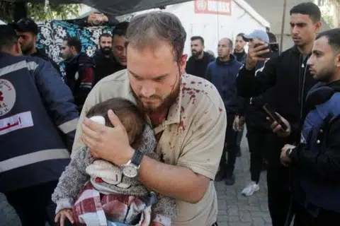 Seorang lelaki Palestin mendukung seorang kanak-kanak yang cedera di sebuah hospital, selepas serangan Israel ke atas sebuah sekolah yang menempatkan penduduk yang dipindahkan di Bandar Gaza. 