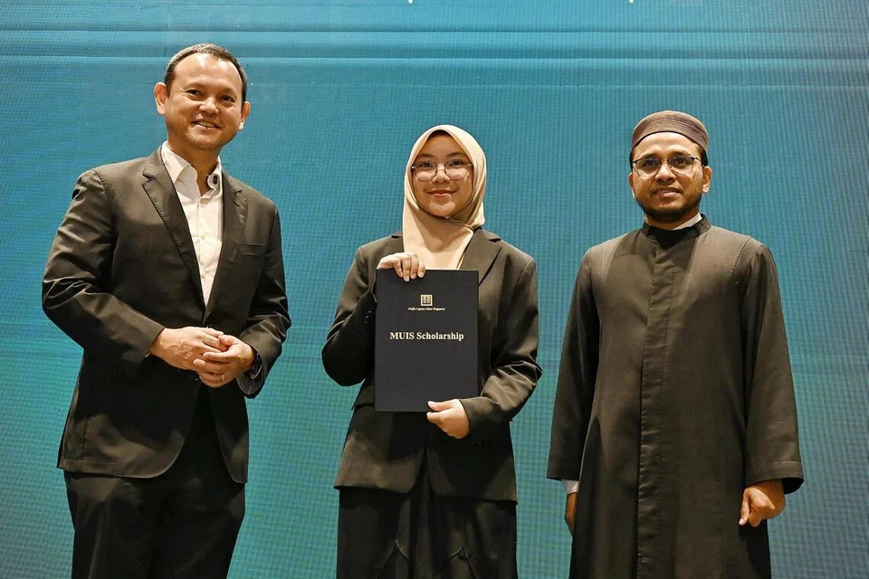 Pelajar Madrasah Aljunied Program Diploma Baccalaureate Antarabangsa, Cik Hannah Yusra Rashid, 19 tahun (tengah), menerima Biasiswa MUIS daripada Pemangku Menteri Bertanggungjawab bagi Ehwal Masyarakat Islam, Encik Zaqy Mohamad (kiri) dan Mufti, Dr Nazirudin Mohd Nasir (kanan) pada 20 Julai.