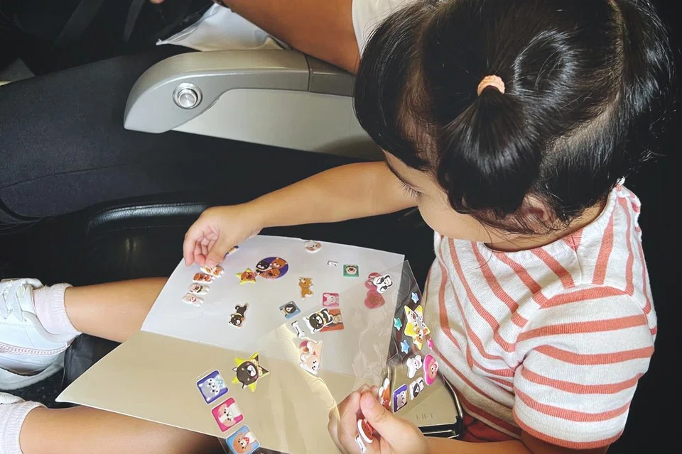 TAMPAL PELEKAT: Anak penulis kelihatan menampal pelekat dalam buku nota kosong bagi menghiburkannya semasa dalam pesawat.