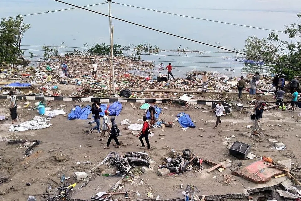BENCANA BERGANDA: Orang ramai lalu lalang di sisi mayat korban yang ditutup dengan kanvas biru sehari selepas gempa bumi dan tsunami melanda Palu di Pulau Sulawesi, Indonesia. - Foto fail AFP