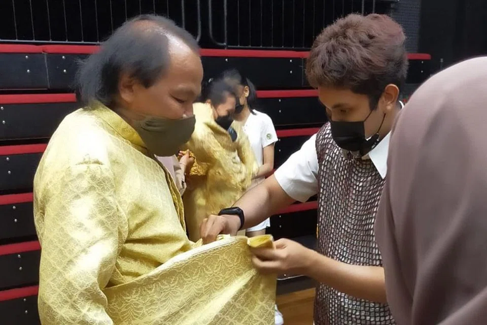 PAKAIAN TRADISIONAL: Pelakon Bangsawan mapan Azman Shariff (kiri) memberi peluang kepada peserta muda bengkel bangsawan menyiapkan beliau untuk watak Raja Iskandar Shah. - Foto ANGGERIK TEMASEK BANGSAWAN. 