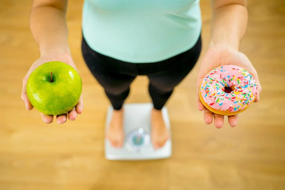 PILIHAN DI TANGAN ANDA: Wanita dengan timbangan berat badan  memegang epal dan donat perlu membuat pilihan antara pencuci mulut makanan tidak sihat dengan yang sihat.