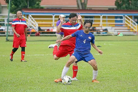 PERLAWANAN PERSAHABATAN: Pemain pasukan CP, Shafiq Ariff (jersi biru), mengawal bola daripada dicuri Anggota Parlimen (AP) Bishan-Toa Payoh GRC, Encik Chong Kee Hiong. Memerhatikan mereka ialah AP Aljunied GRC, Encik Faizal Manap. - Foto THE STRAITS TIMES