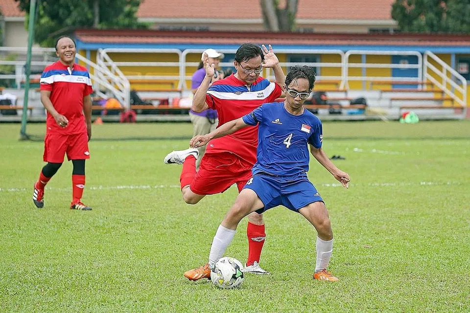 PERLAWANAN PERSAHABATAN: Pemain pasukan CP, Shafiq Ariff (jersi biru), mengawal bola daripada dicuri Anggota Parlimen (AP) Bishan-Toa Payoh GRC, Encik Chong Kee Hiong. Memerhatikan mereka ialah AP Aljunied GRC, Encik Faizal Manap. - Foto THE STRAITS TIMES