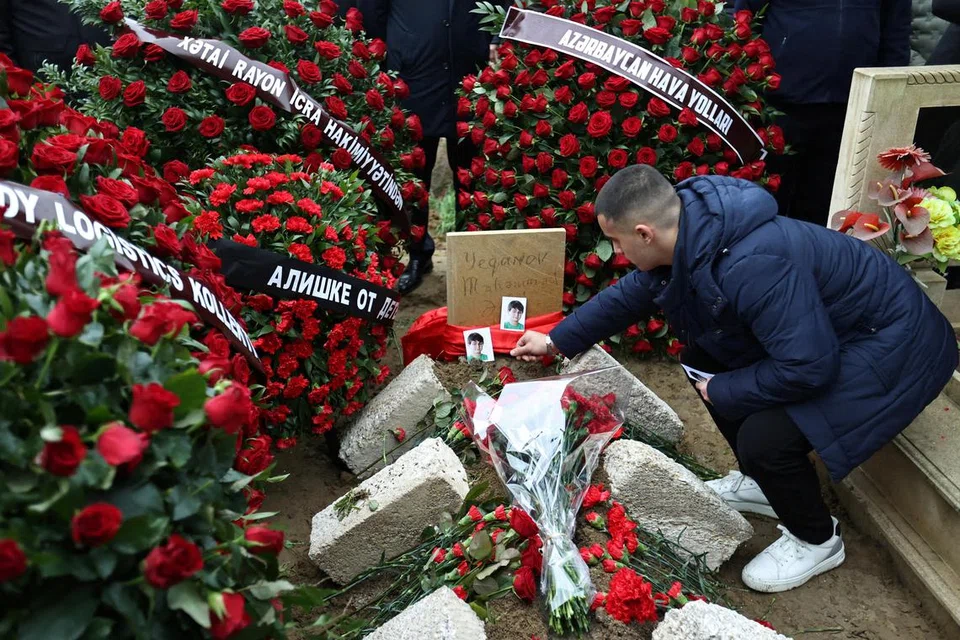 Seorang lelaki meletakkan gambar mangsa nahas pesawat, Mahammadali Eganov, 13 tahun, di kuburnya di Baku, Azerbaijan, pada 28 Disember.