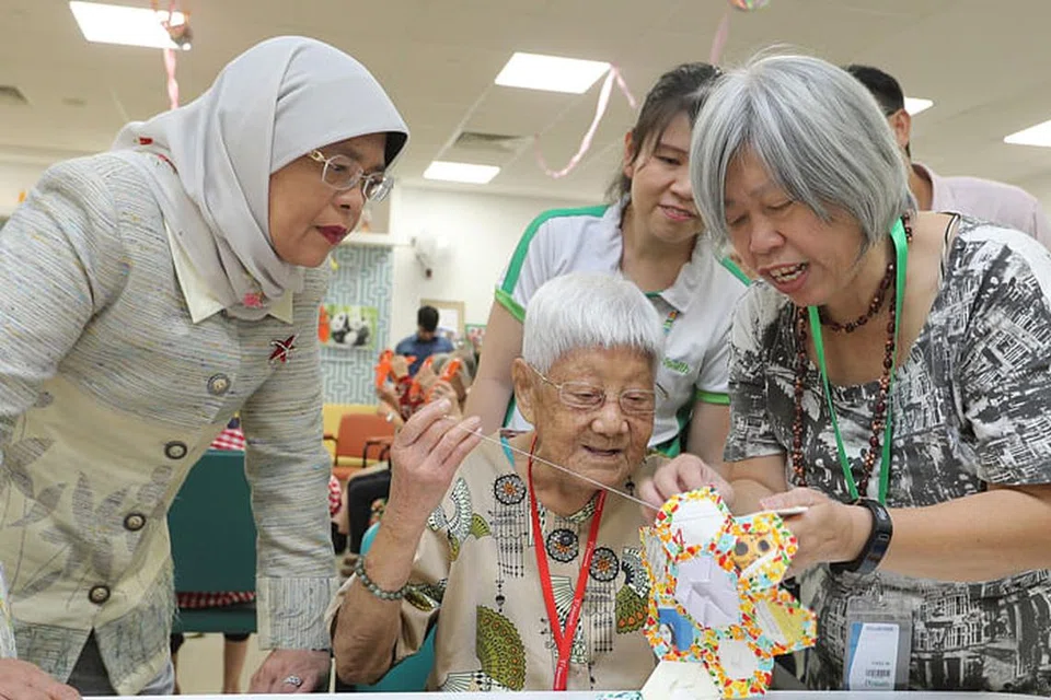TEKUN TELITI: Puan Halimah menyaksikan penduduk, Cik Leong Hup Sow, yang masih lagi mahir dan teliti melakukan kerja tampal cantum (patchwork) walaupun beliau sudah berusia 91 tahun semasa lawatannya ke Kampung Admiralty semalam. - Foto MCI