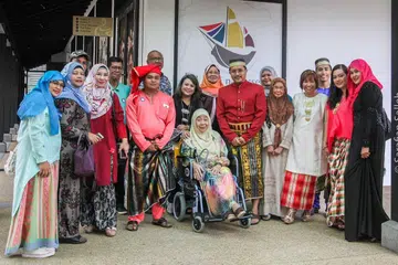 MEMPERAGA BUSANA BUGIS: Orang Bugis Singapura masih berbangga menggayakan busana Bugis di khalayak ramai semasa mengunjungi pameran 'Sirri Na Pesse: Menelusuri Identiti Masyarakat Bugis di Singapura' dari 14 Oktober 2017 hingga 24 Jun 2018. Saya pula (berdiri di tengah) mengenakan baju berwarna merah pekat, berkain dam bersongkok pakaian di sebelah mantan Wanita Pertama Singapura, Puan Noor Aishah, yang turut menyaksikan pameran itu di Taman Warisan Singapura. - Foto ihsan SARAFIAN SALLEH