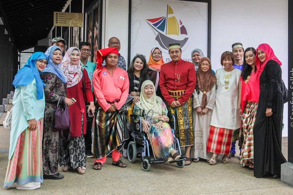 MEMPERAGA BUSANA BUGIS: Orang Bugis Singapura masih berbangga menggayakan busana Bugis di khalayak ramai semasa mengunjungi pameran 'Sirri Na Pesse: Menelusuri Identiti Masyarakat Bugis di Singapura' dari 14 Oktober 2017 hingga 24 Jun 2018. Saya pula (berdiri di tengah) mengenakan baju berwarna merah pekat, berkain dam bersongkok pakaian di sebelah mantan Wanita Pertama Singapura, Puan Noor Aishah, yang turut menyaksikan pameran itu di Taman Warisan Singapura. - Foto ihsan SARAFIAN SALLEH