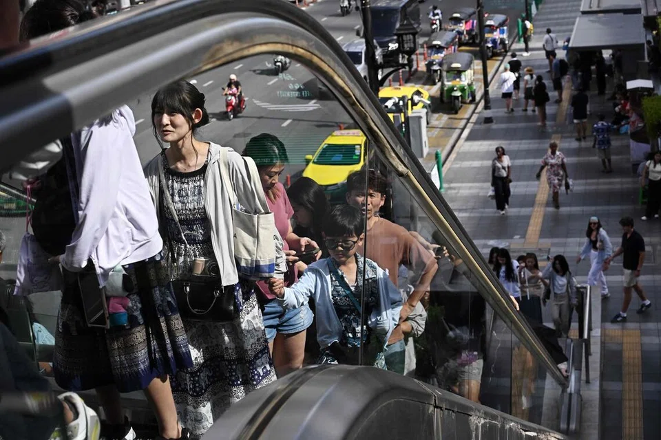 Pedestrians take an escalator in Pathum Wan shopping district in Bangkok on June 22, 2026. (Photo by Lillian SUWANRUMPHA / AFP)