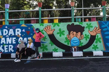 KEKHUATIRAN TERASA: Menteri Pengangkutan Indonesia, Encik Budi Kareya Sumadi menjangkakan penghijrahan besar-besaran atau pulangnya penduduk ke kampung masing-masing apabila bermulanya cuti lima hari pada Rabu ini (28 Oktober) sempena sambutan Maulidur Rasul di Indonesia.Ini antara kekhuatiran yang dirasakan seandainya jumlah jangkitan baru Covid-19 bertambah. Foto hiasan ini dirakam di Surabaya dengan mural yang menggalak orang ramai menggunakan pelitup muka dipaparkan. - Foto AFP