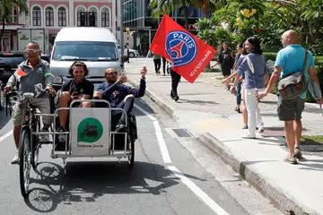 SERONOK JALAN-JALAN: Dua pemain PSG, Adrien Rabiot (tengah) dan Lyvin Kurzawa (memegang bendera PSG) mengambil peluang ketika waktu lapang mereka untuk bersiar-siar mengelilingi Singapura dengan menaiki beca. Mereka juga sempat mencuba beberapa hidangan tempatan seperti membuat prata dan memakan durian. - Foto PSG 