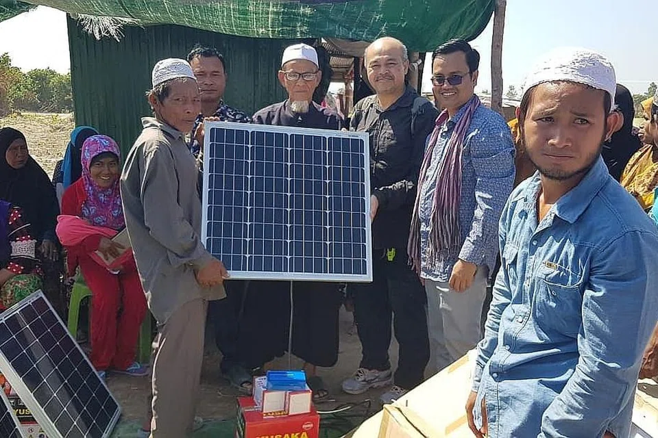 KINI HIDUP TERANG-BENDERANG: Encik Ismail (berdiri, empat dari kiri) bersama penduduk yang baru menerima salah satu daripada 30 panel solar sumbangan sekumpulan warga Singapura. - Foto ihsan ISMAIL ABU BAKAR