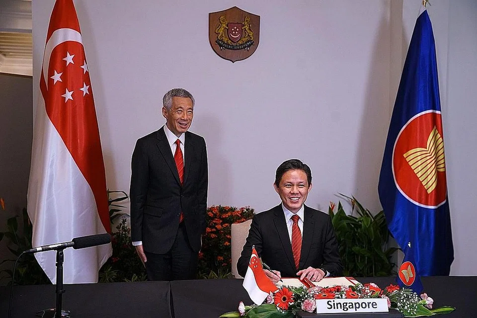 DEMI KEMAJUAN EKONOMI: Menteri Perdagangan dan Perusahaan Chan Chun Sing (duduk) menandatangani perjanjian Kerjasama Ekonomi Menyeluruh Serantau (RCEP) yang melibatkan 15 negara sambil disaksikan Perdana Menteri Lee Hsien Loong (kiri) dan pemimpin negara lain menerusi video semalam. Majlis itu sebahagian Puncak Asean ke-37 dan persidangan berkaitan. - Foto MCI