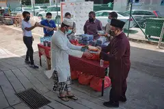 PENGAGIHAN DI DORMITORI: Seorang pekerja asing menerima makanan serta kain sarong daripada Timbalan Mufti Dr Hannan (kanan) di dormitori Tuas View Square kelmarin. - Foto BH oleh JASON QUAH