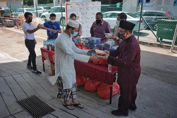 PENGAGIHAN DI DORMITORI: Seorang pekerja asing menerima makanan serta kain sarong daripada Timbalan Mufti Dr Hannan (kanan) di dormitori Tuas View Square kelmarin. - Foto BH oleh JASON QUAH