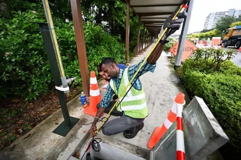 Seorang kontraktor, ditemani pegawai PUB, mengukur kabel penderia paras air selepas menguji ketepatannya di sebelah saluran air di Bukit Timah Road pada 25 November.
