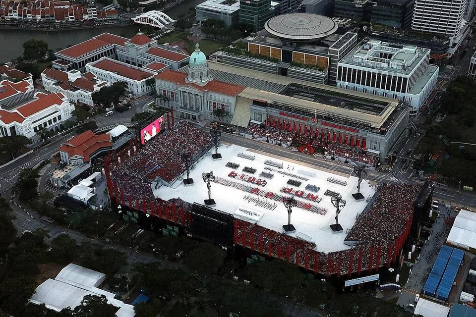 LAUTAN MERAH PUTIH: Pemandangan Padang dari udara ketika lagu kebangsaan dimainkan. Warga Singapura bersatu hati, berdiri sambil menyanyikan 'Majulah Singapura' sambil bendera negara dikibarkan secara terbang lalu. Lagu kebangsaan dinyanyikan selepas kontinjen Perbarisan dan Upacara (P&C) mengambil tempat masing-masing di Padang. - Foto SPH