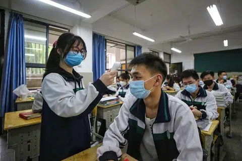 JAGA SEKITARAN: Seorang pelajar menengah memeriksa suhu badan rakan sedarjah sebelum kelas bermula di sebuah sekolah di Wuhan, wilayah Hubei, China pada 6 Mei lalu. 
