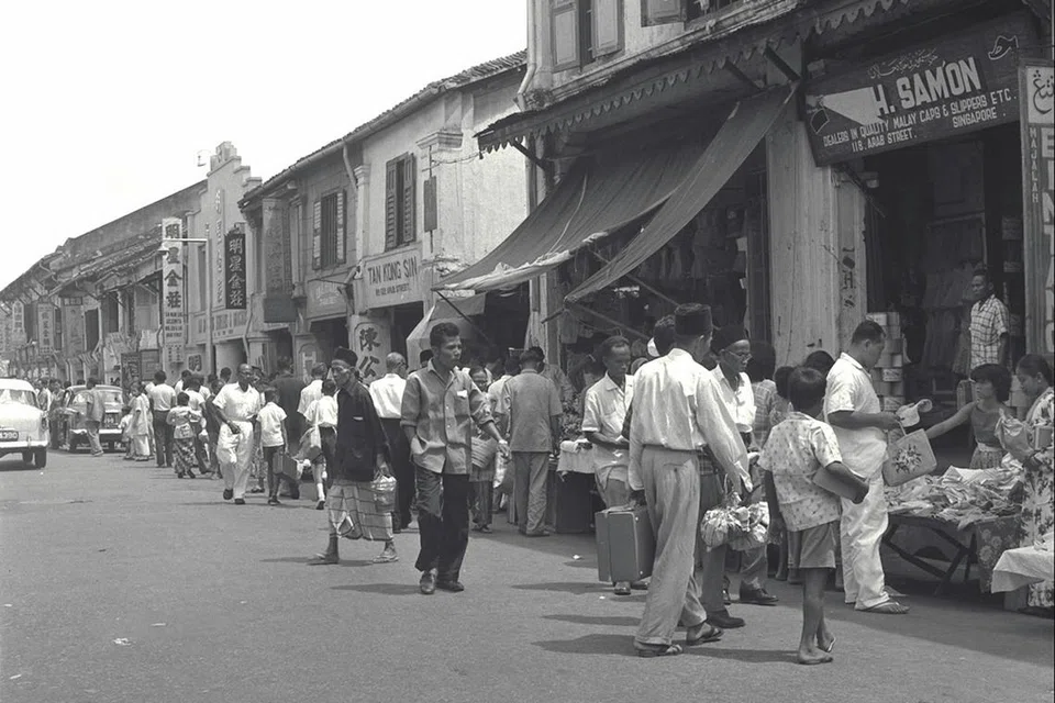 Orang ramai bergegas ke kedai-kedai pakaian dan makanan di Arab Street untuk membeli-belah bagi menyambut Hari Raya selepas waktu kerja tamat. Gambar ini dipetik pada 26 Mac 1960. 