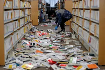 KESAN GEMPA: Seorang pekerja perpustakaan di Jepun sedang membersihkan buku-buku yang bersepahan menyusuli gempa bumi teruk pada tengah malam Sabtu. - Foto REUTERS/ISSEI KATO
