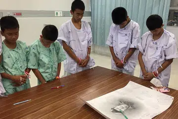 KENANG JASA PENYELAMAT TERKORBAN: Sebahagian anggota pasukan bola sepak Wild Boars yang diselamatkan dan sedang menjalani rawatan di Hospital Prachanukroh bertafakur bagi mengenang jasa seorang penyelamat, mendiang Samarn Kunan, (wajah yang dilukis, atas meja), yang maut semasa menjalankan usaha menyelamat 12 remaja itu dan seorang jurulatih mereka. - Foto REUTERS