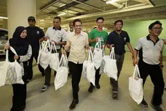 RAMAI-RAMAI MEMBANTU: Dr Maliki (tengah) dan kakitangan 4PM termasuk Presiden, Encik Izzuddin Taherally (empat dari kiri), Ketua Negara Grab, Encik Wee Tang (tiga dari kanan) dan sukarelawan membantu membawa beg habuan yang turut termasuk biskut Raya yang kemudian diagihkan kepada para penerima bantuan. - Foto BH oleh ROSLEE ABDUL RAZAK