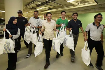 RAMAI-RAMAI MEMBANTU: Dr Maliki (tengah) dan kakitangan 4PM termasuk Presiden, Encik Izzuddin Taherally (empat dari kiri), Ketua Negara Grab, Encik Wee Tang (tiga dari kanan) dan sukarelawan membantu membawa beg habuan yang turut termasuk biskut Raya yang kemudian diagihkan kepada para penerima bantuan. - Foto BH oleh ROSLEE ABDUL RAZAK