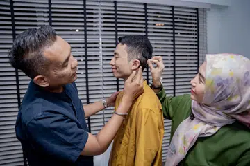 DAPAT DIKESAN AWAL: Masalah pendengaran Justin Absar, 17 tahun (tengah), dikenal pasti sejak dia bayi. Mujur ibu bapanya, Encik Muhammad Sofian Ahmad dan Cik Jecky Augustine Johansyah, membuat keputusan membuat pembedahan implan koklea baginya ketika anak mereka itu berusia 18 bulan.