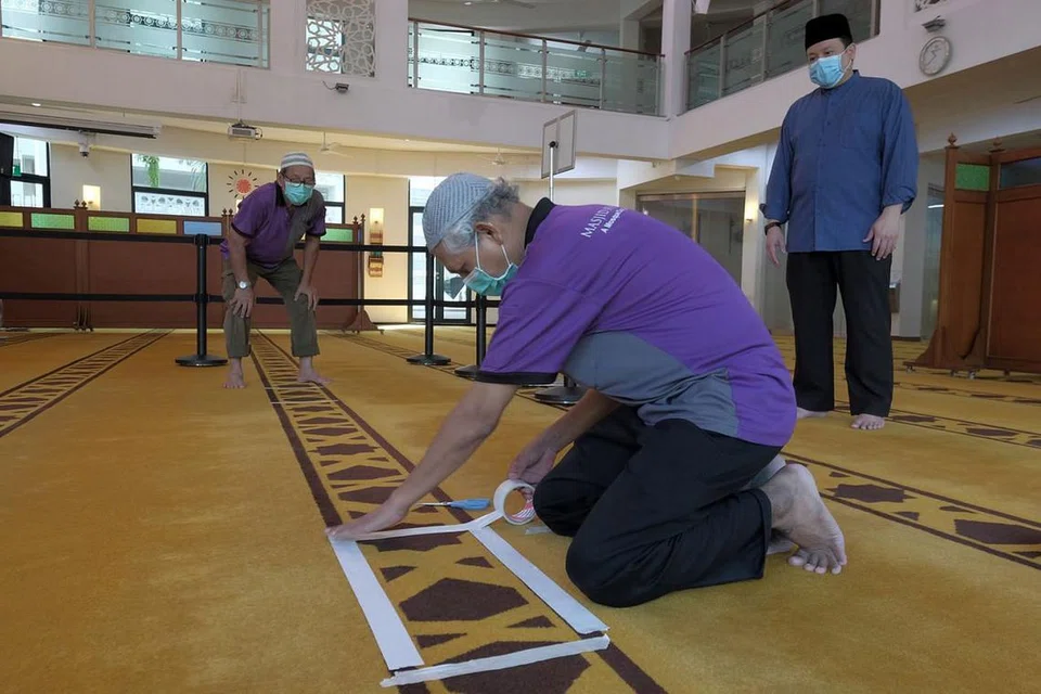 PERSIAPAN BERJALAN LANCAR: Seorang kakitangan Masjid Mujahidin melekatkan pelekat putih di permaidani dewan solat. Jemaah individu diminta berdiri di dalam kotak ini semasa menunaikan ibadah. - Foto BH oleh GAVIN FOO