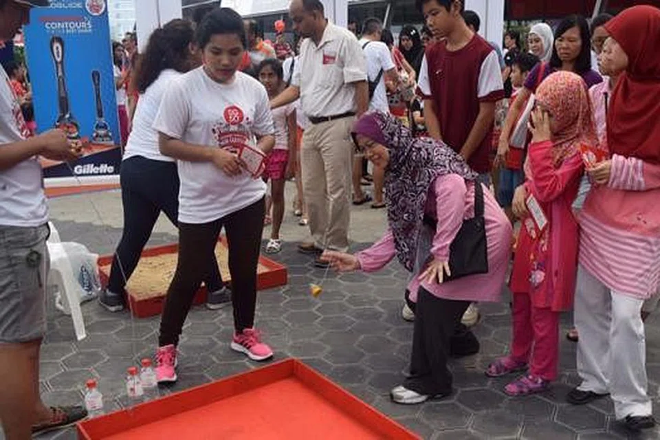 PERMAINAN TRADISIONAL: Cik Zainab Abdul Rashid (tiga dari kanan) menunjukkan teknik melontar gasing kepada anak-anaknya (dari kanan), Dinah Aziz dan Soffyah Aziz.