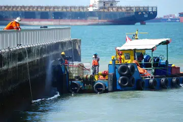 Seorang pekerja sedang membersihkan tembok di Pantai Easi Coast menggunakan bot pembersih. 