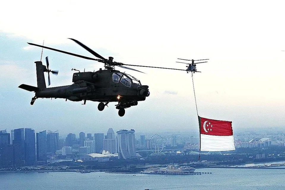 BERKIBAR MEGAH: Bendera Singapura dikibar megah dari helikopter Chinook berlatarbelakangkan bangunan pencakar langit Singapura seperti Marina Bay Sands dan Singapore Flyer. Bendera Singapura dikibar selama 16 saat di atas Padang sambil lagu kebangsaan dimainkan. - Foto SPH